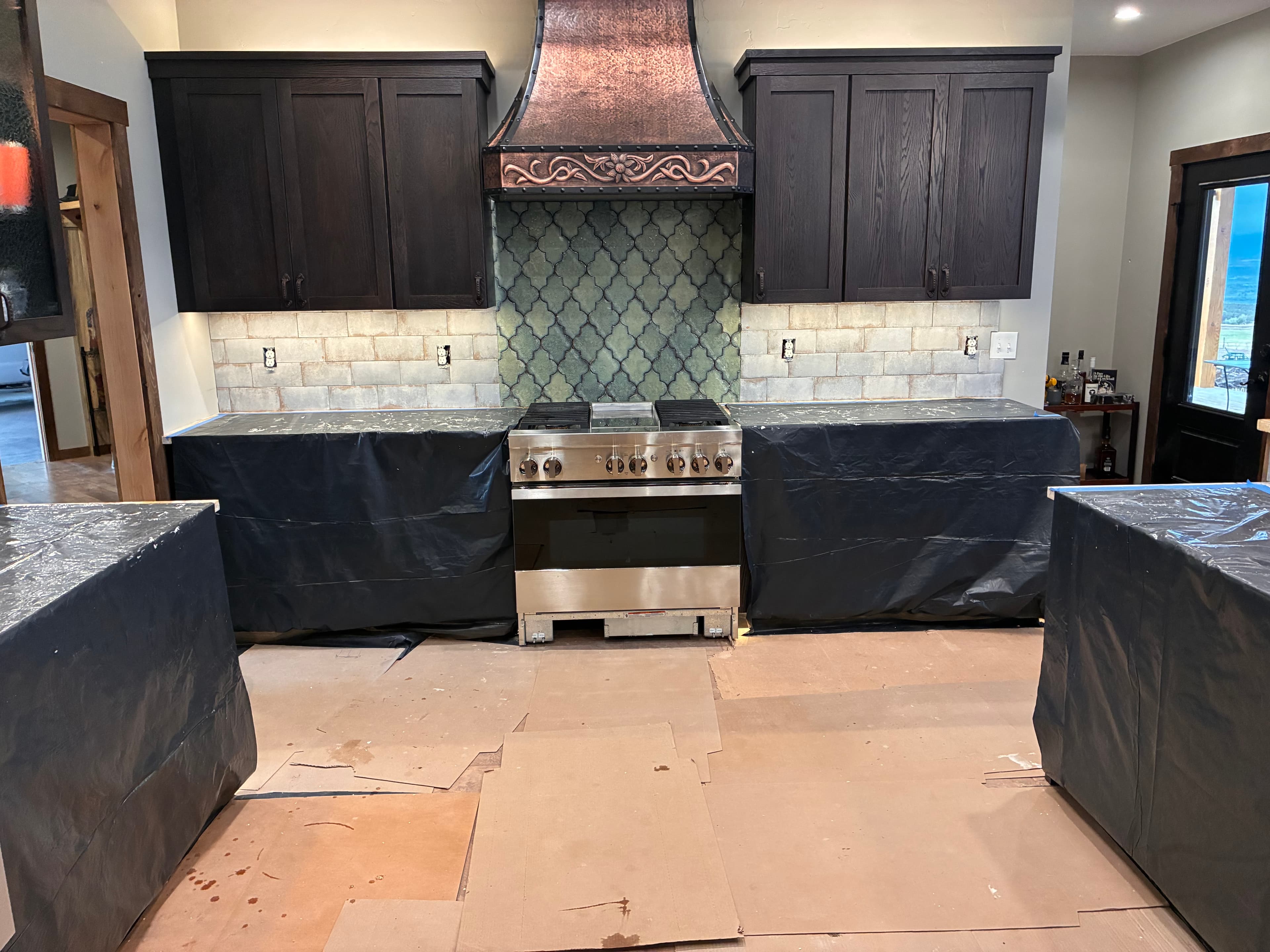 Kitchen renovation featuring dark cabinets, ornate copper range hood, and green arabesque tile backsplash.