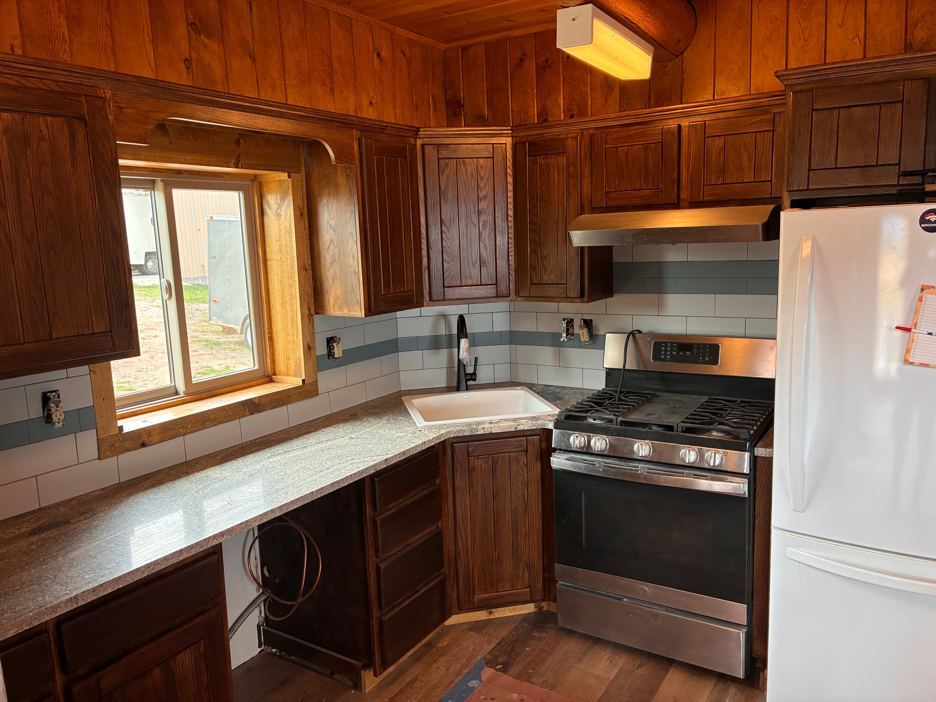 Rustic kitchen with dark wood cabinets, granite countertops, white corner sink, and stainless steel range.