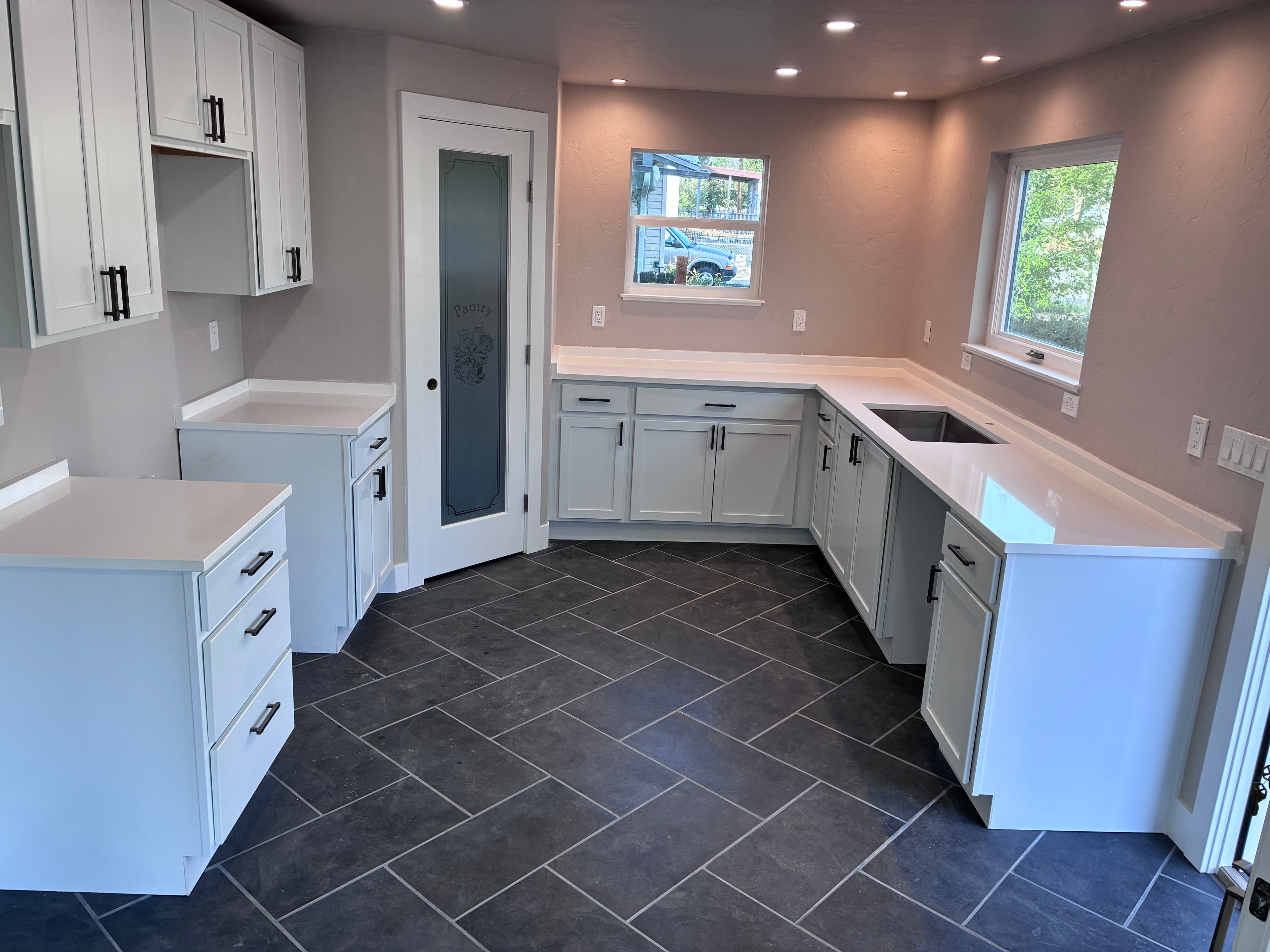 Modern kitchen featuring white cabinets, black hardware, white countertops, and dark grey tile flooring.