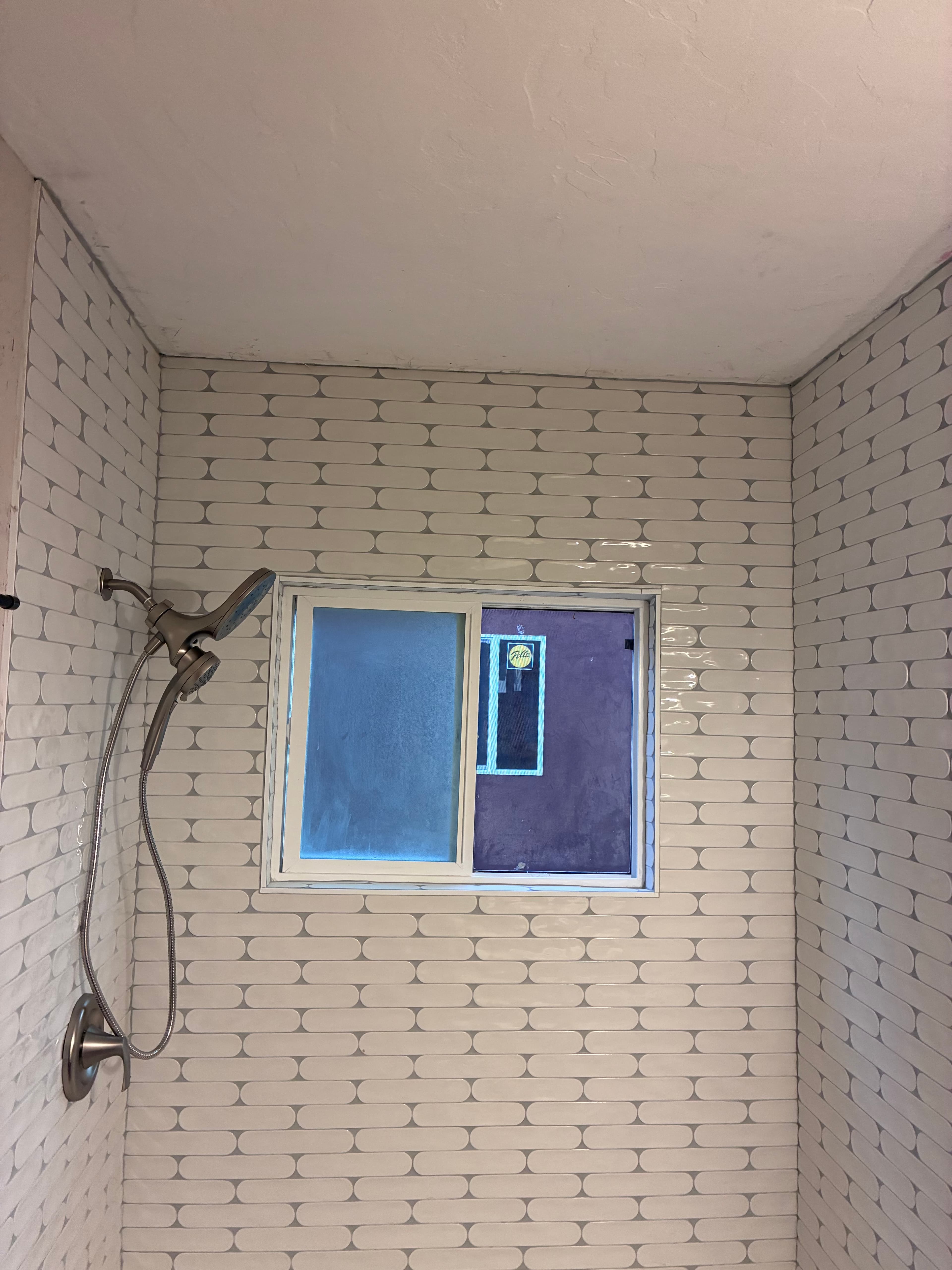 White pill-shaped tiled shower with a brushed nickel shower head and a small window.