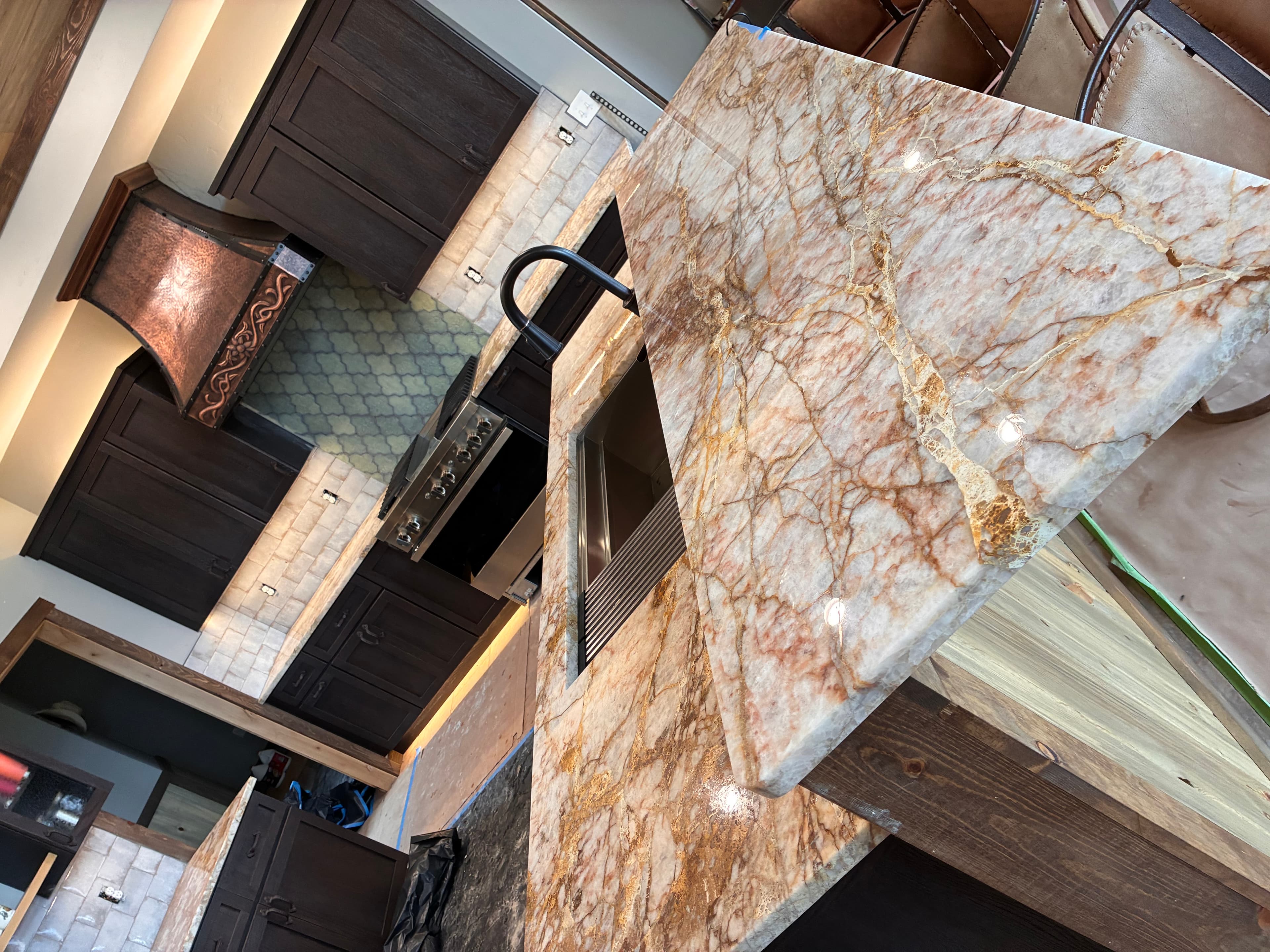 Kitchen with a gold-veined marble island, dark wood cabinets, and a decorative copper hood.